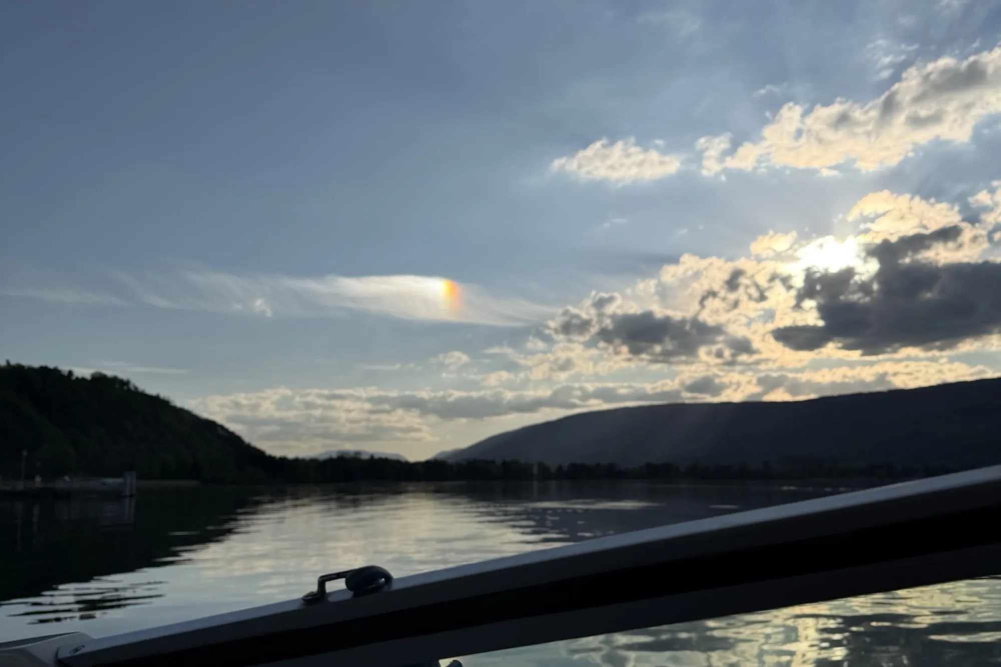 Blick von Bord über den See auf eine bewaldete Hügelkette im Abendlicht.